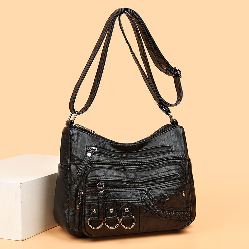 Black leather handbag with multiple zippers on a beige background