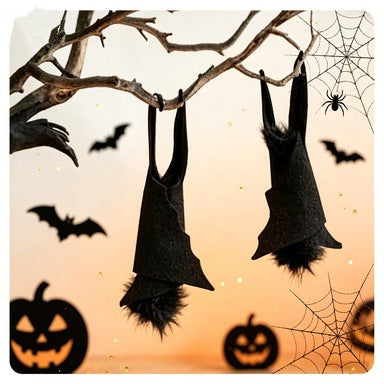 Halloween bat decorations hanging from a bare tree branch against an orange sunset background, with silhouettes of bats, jack-o'-lanterns, and spiderwebs.