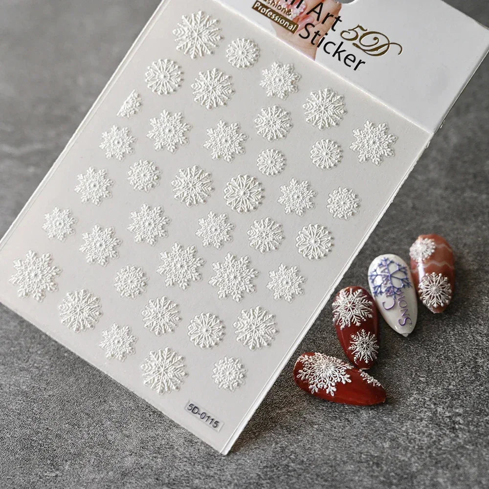 Sheet of white 3D snowflake nail art stickers on gray background with decorated false nails.