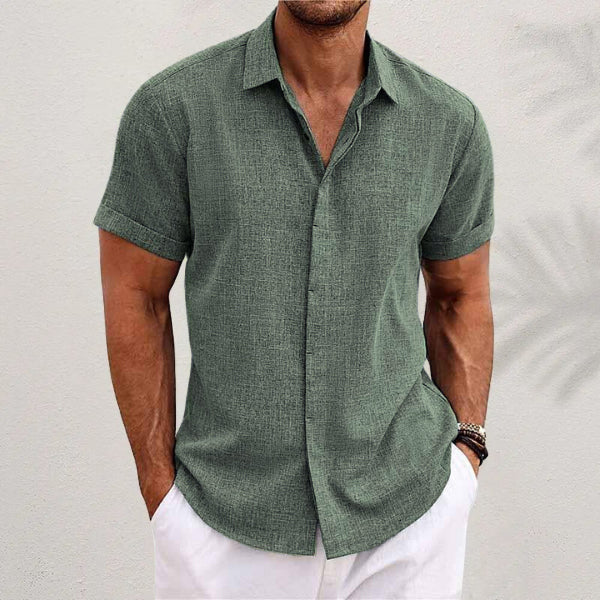 Man wearing a green short-sleeve shirt and white pants against a light gray background