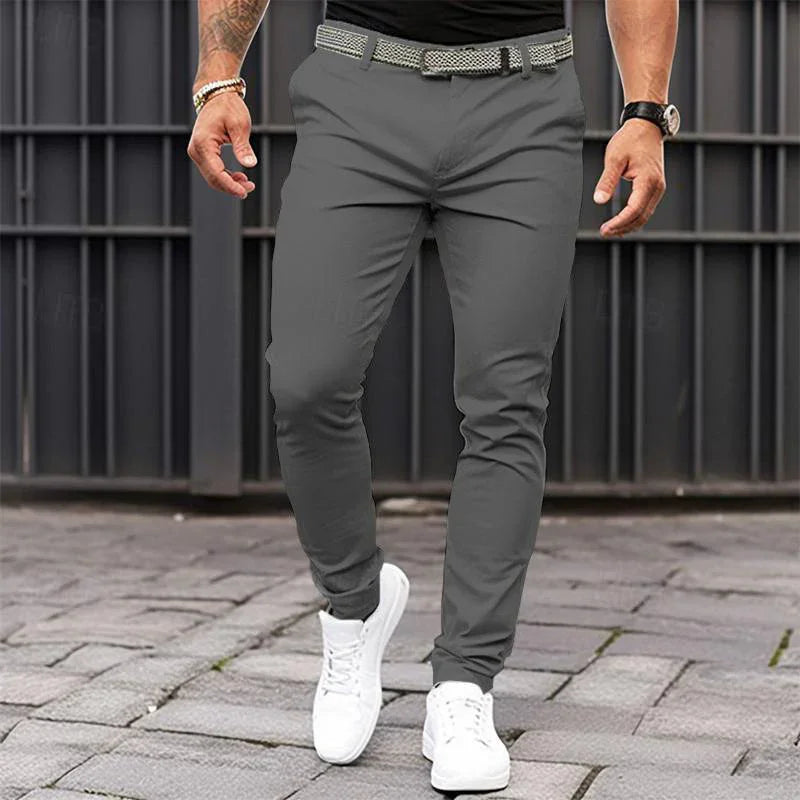 Person wearing gray pants and white sneakers on a paved surface with a metal gate background