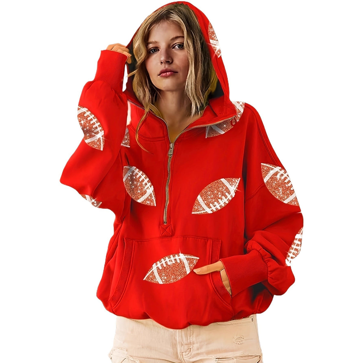 A woman wearing a bright red half-zip hoodie with football-shaped sequin patches on the front and sleeves, paired with light beige pants, set against a plain white background.