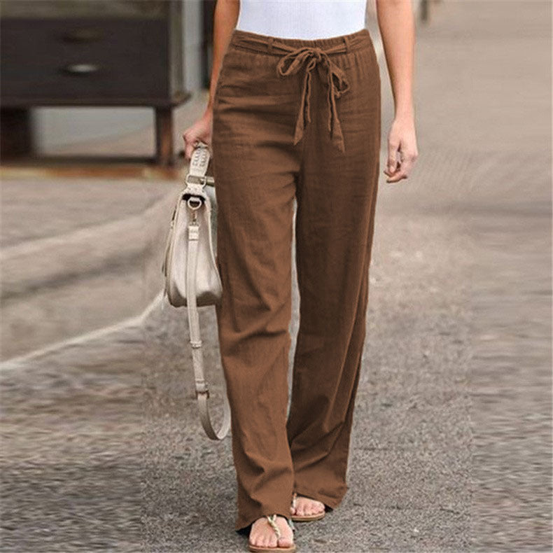 Person wearing brown pants holding a beige handbag on a street.