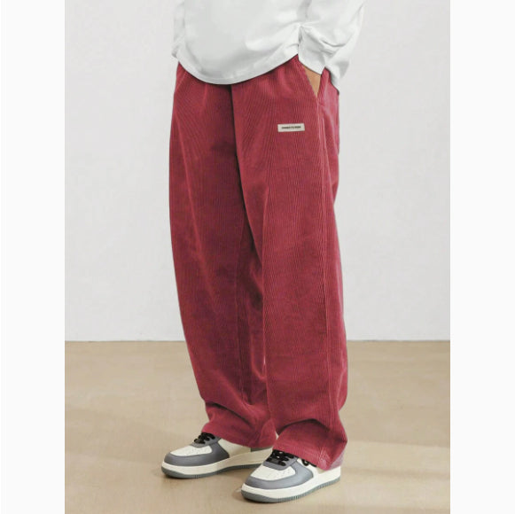 Person wearing red corduroy pants with a white shirt and gray sneakers on a plain background