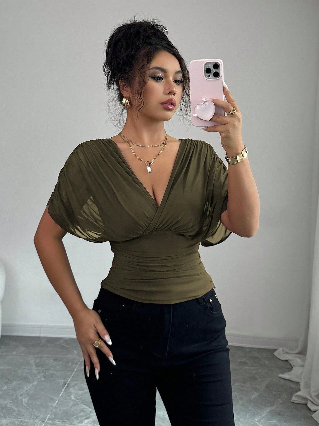 Woman taking a mirror selfie wearing an olive green top and black pants.