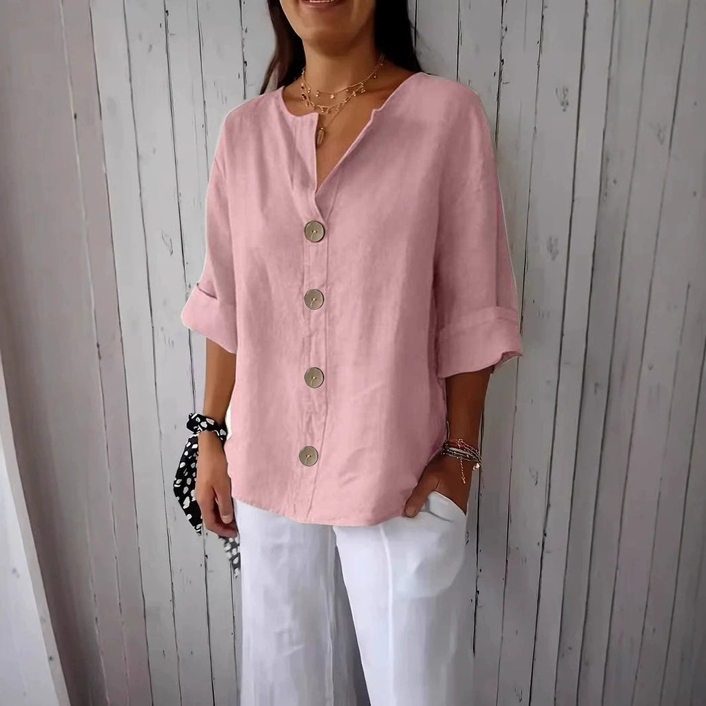 Person wearing a pink button-up shirt and white pants against a wooden background