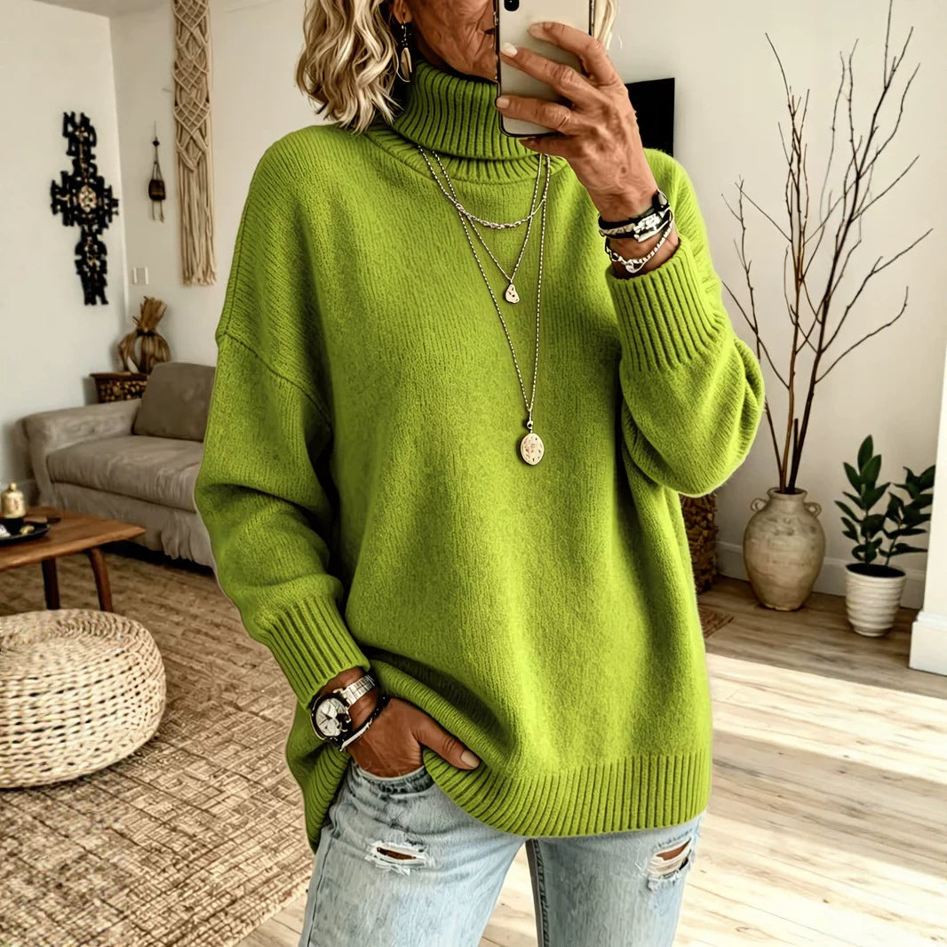 A woman takes a mirror selfie in a cozy living room, wearing an oversized bright lime green turtleneck sweater, distressed light blue jeans, and layered silver necklaces.