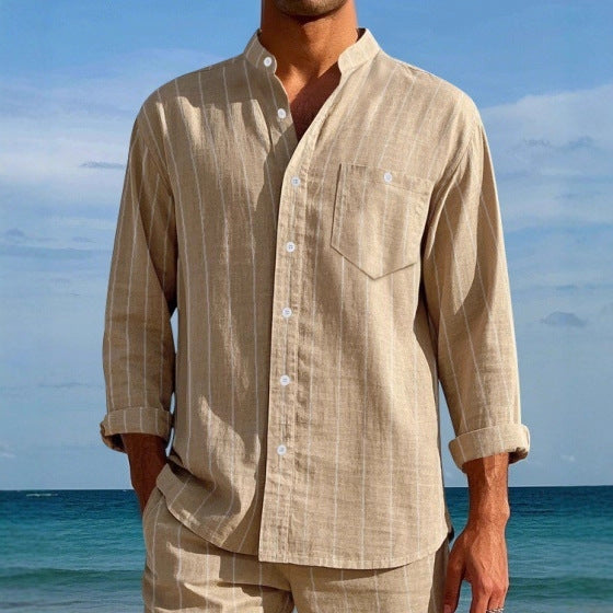 Man wearing a beige shirt and pants standing by the ocean with a clear blue sky.