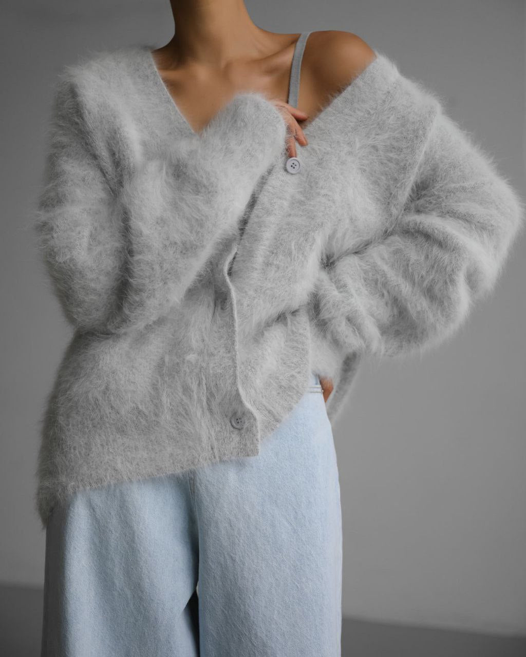 Person wearing a fluffy gray cardigan and light blue pants against a neutral background
