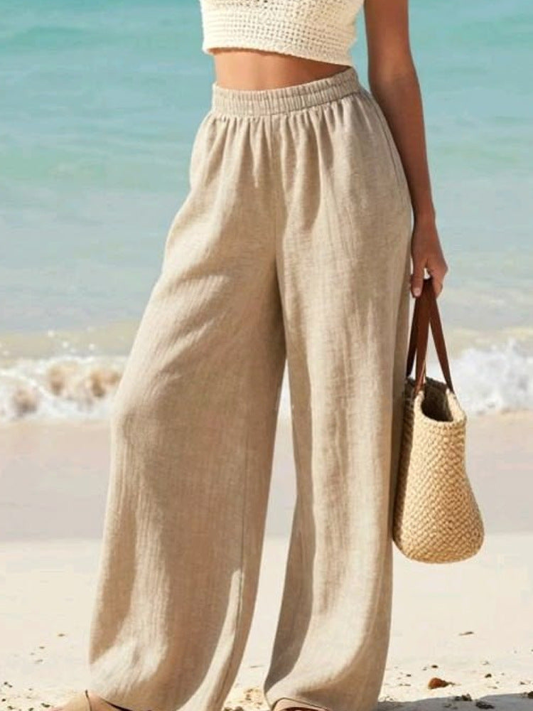Person wearing beige wide-leg pants on a beach with a blurred ocean background