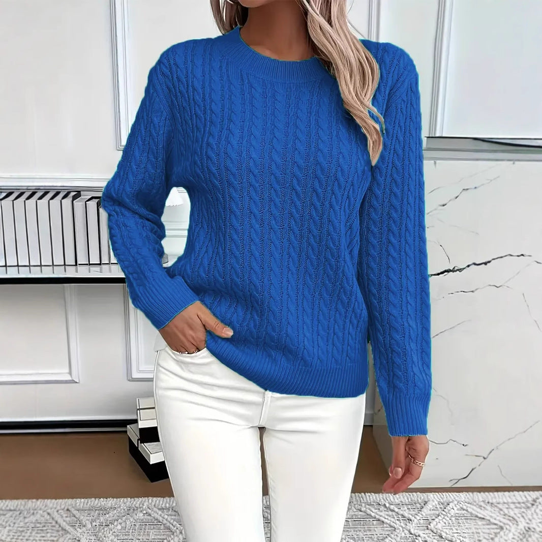 Person wearing a blue cable knit sweater and white pants in a room with a marble wall.