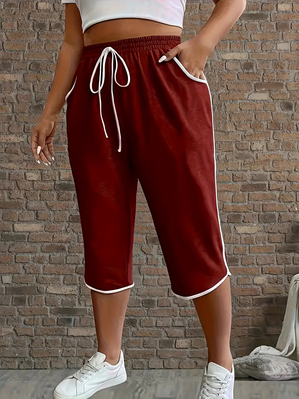 Person wearing maroon capri pants with white trim against a brick wall.