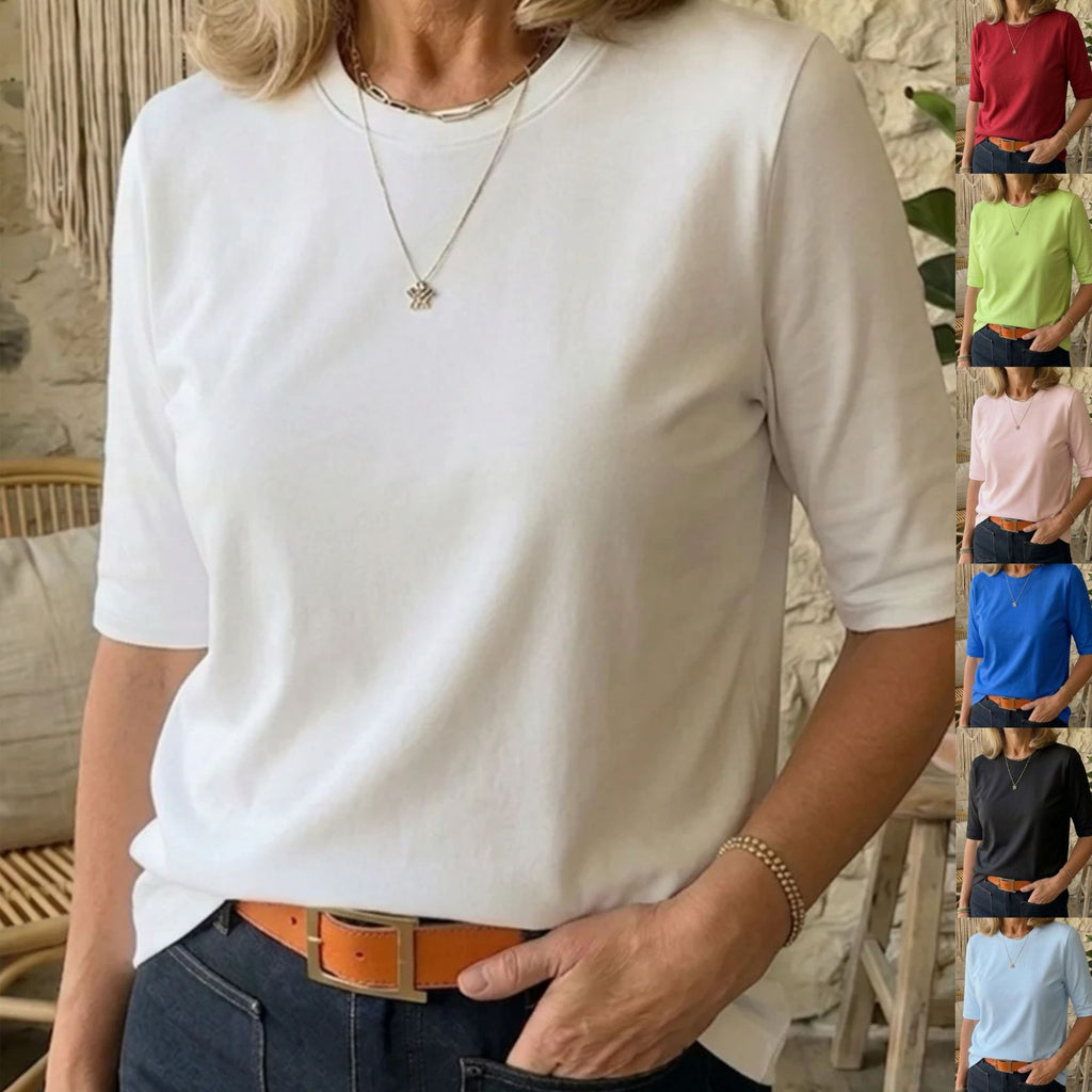 A woman wearing a white short-sleeve crewneck t-shirt, styled with dark blue jeans and an orange-brown belt. The image features a vertical strip of smaller color options on the right side showing the t-shirt in red, green, pink, blue, black, and light blue.