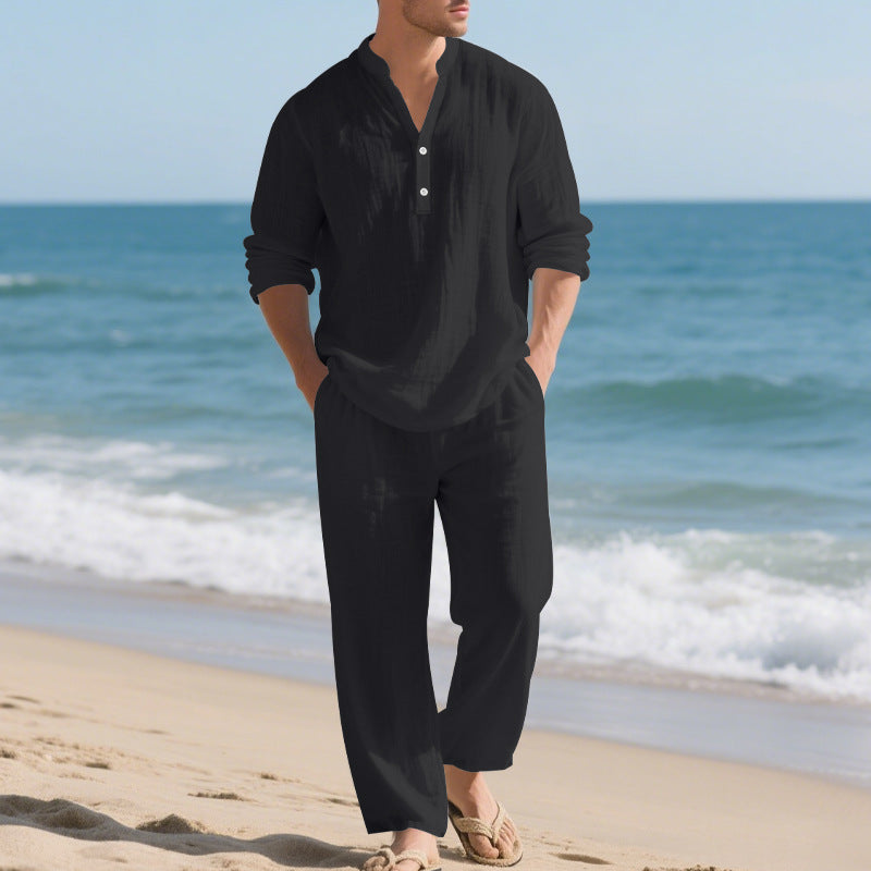 Man wearing a black outfit standing on a beach with ocean waves in the background