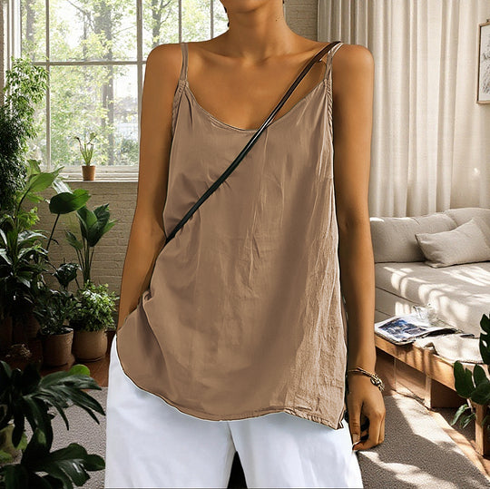 Woman wearing a beige tank top and white pants in a bright living room with plants and a couch.