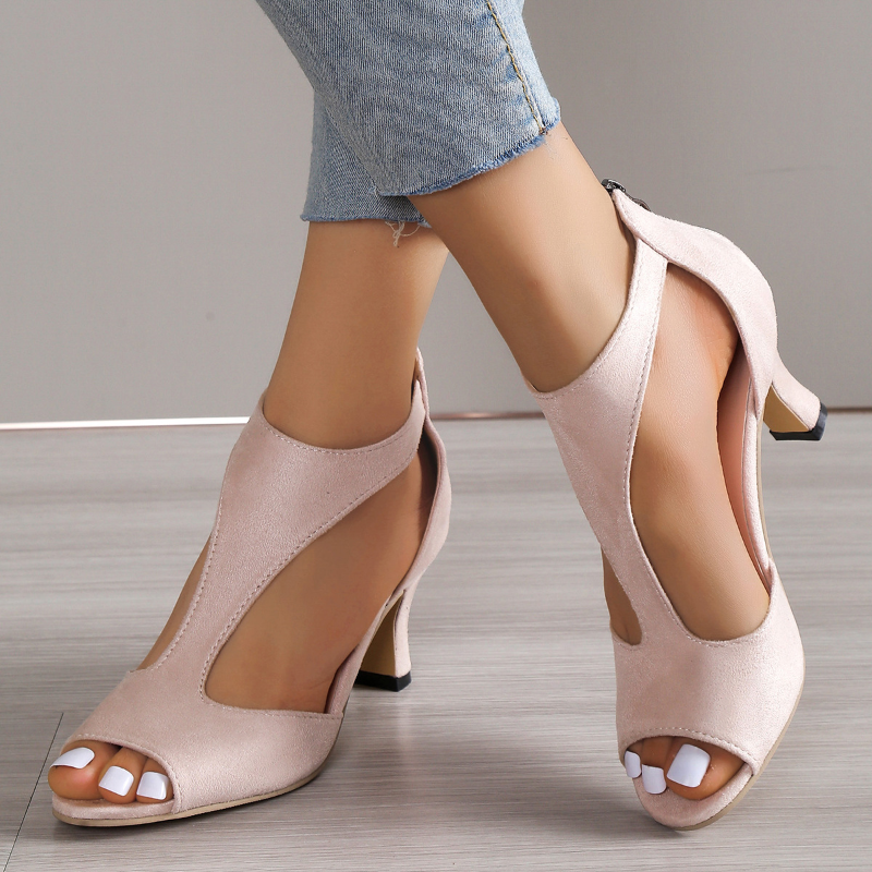 Beige high-heeled shoes worn with denim jeans on a neutral background