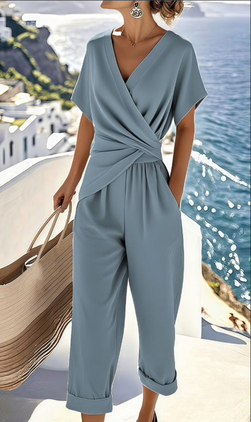 Woman wearing a light blue jumpsuit with a scenic background of water and buildings.