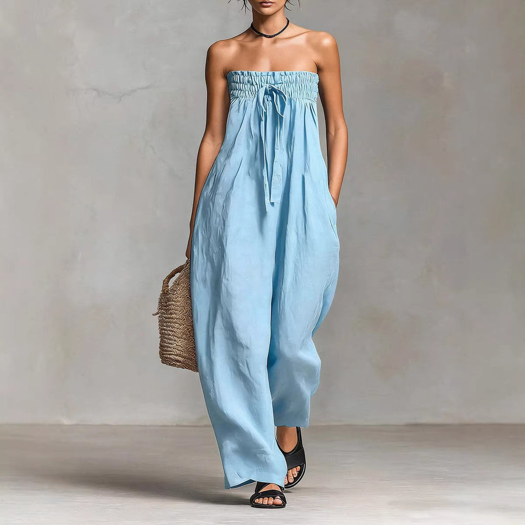 Woman wearing a light blue strapless jumpsuit holding a woven bag against a neutral background