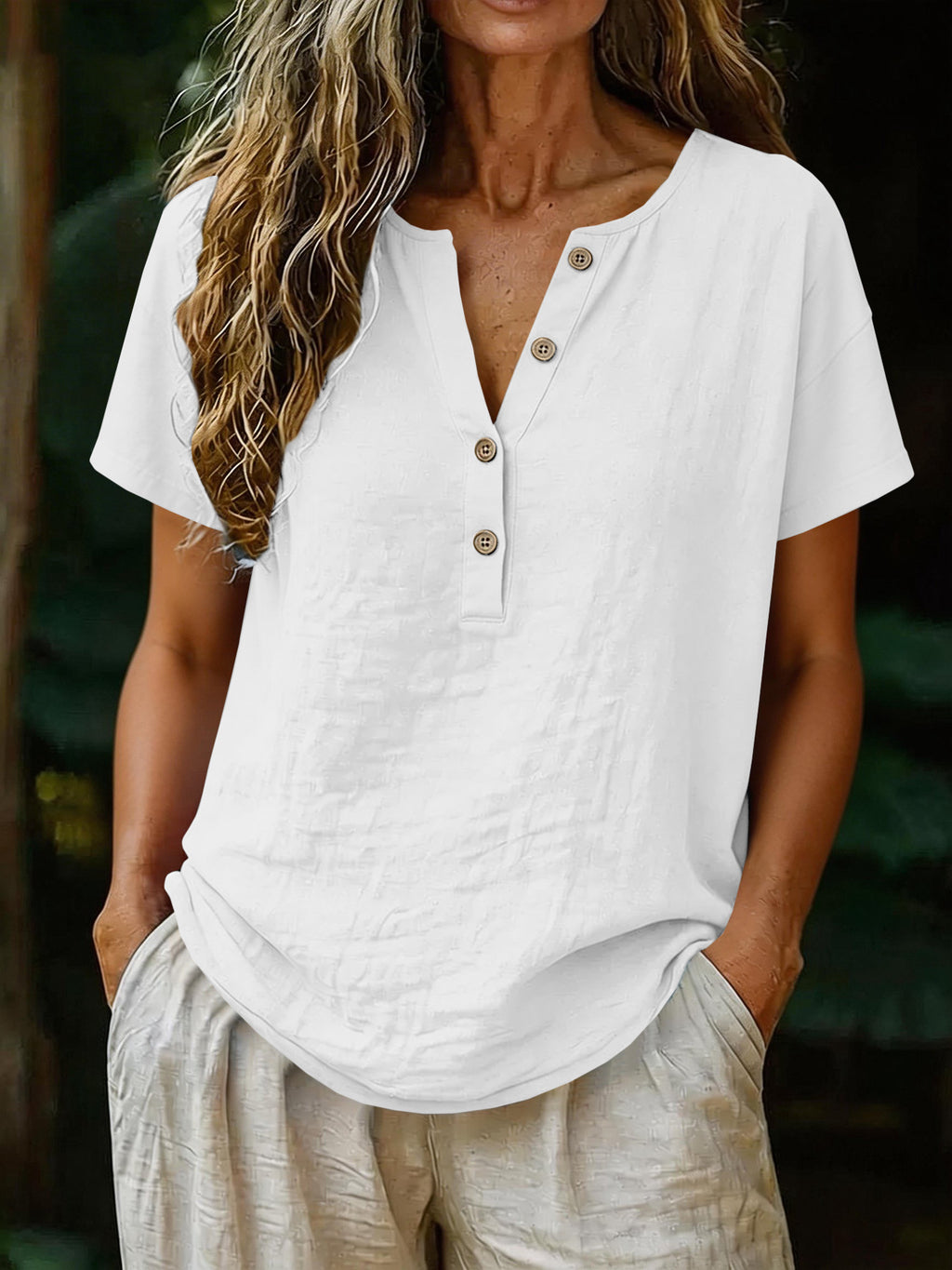 Person wearing a white short-sleeve button-up shirt with beige pants against a blurred natural background