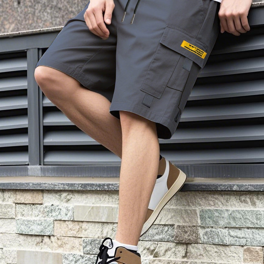Person wearing dark gray cargo shorts with a brand label, sitting on a stone ledge.