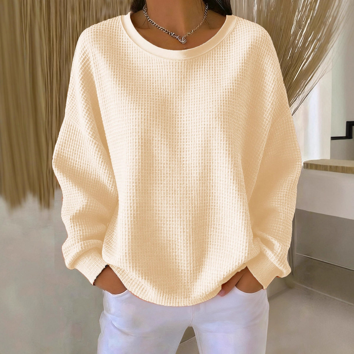 Person wearing a beige sweater and white pants in an indoor setting