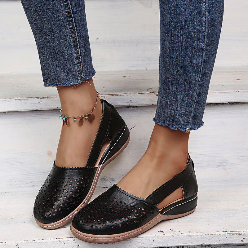 Black perforated loafers worn with blue jeans on a light wooden floor.