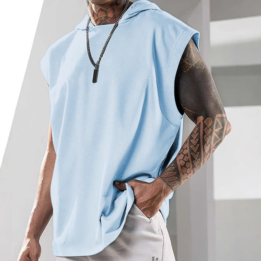 Person wearing a light blue sleeveless hoodie with tattoos on arms, standing against a neutral background.