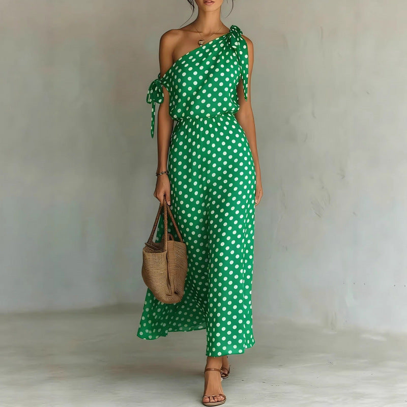 Woman wearing a green polka dot dress holding a woven bag against a plain background