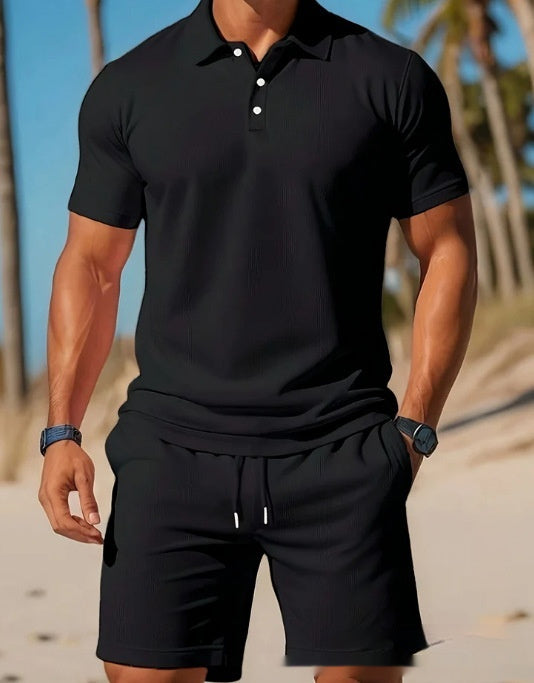 Man wearing a black polo shirt and shorts on a beach.
