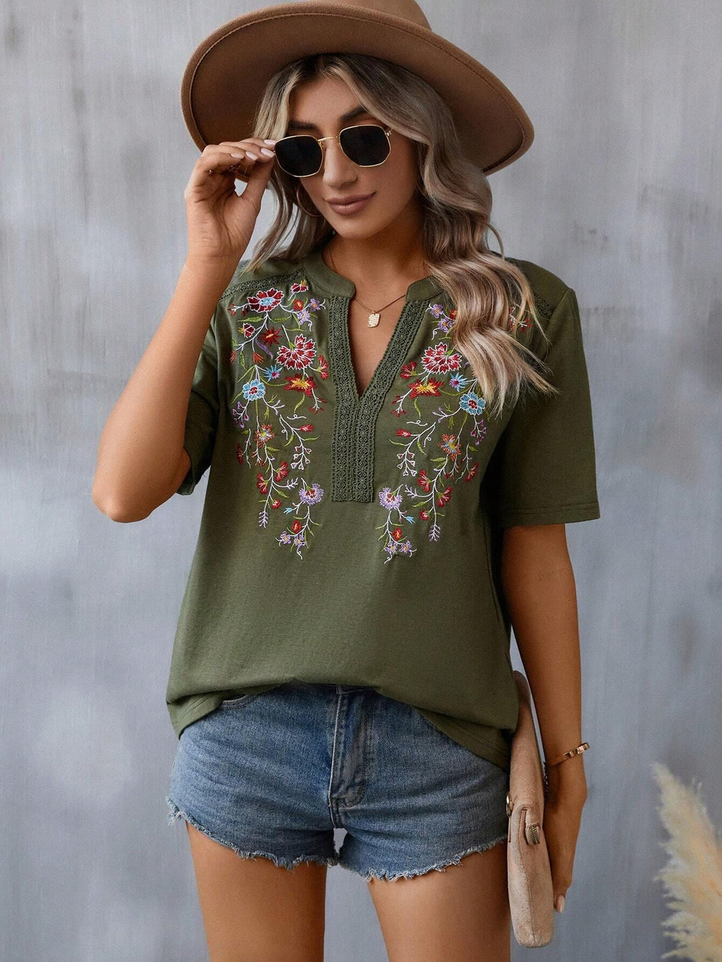 Woman wearing a green embroidered shirt and denim shorts against a gray background