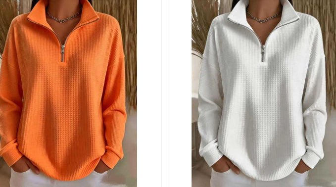 Two women modeling the same quarter-zip long-sleeve waffle-knit top, shown side by side in orange on the left and white on the right, against a neutral indoor backdrop with dried grass decor.