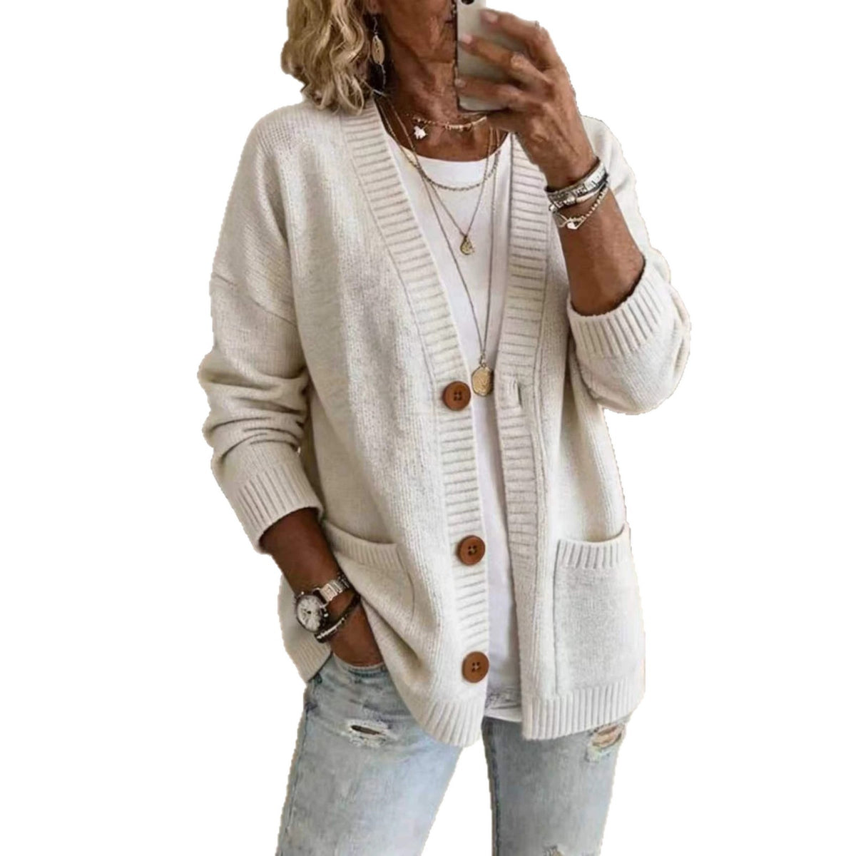 A woman wearing a cream-colored knit cardigan sweater with brown wooden buttons, layered over a white t-shirt and paired with light-wash distressed jeans, shown in a mirror selfie style against a plain white background.