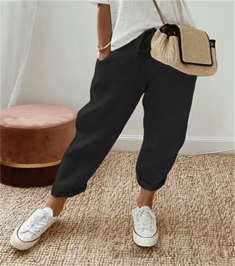 Person wearing black pants and white sneakers with a straw bag, standing on a carpeted floor.