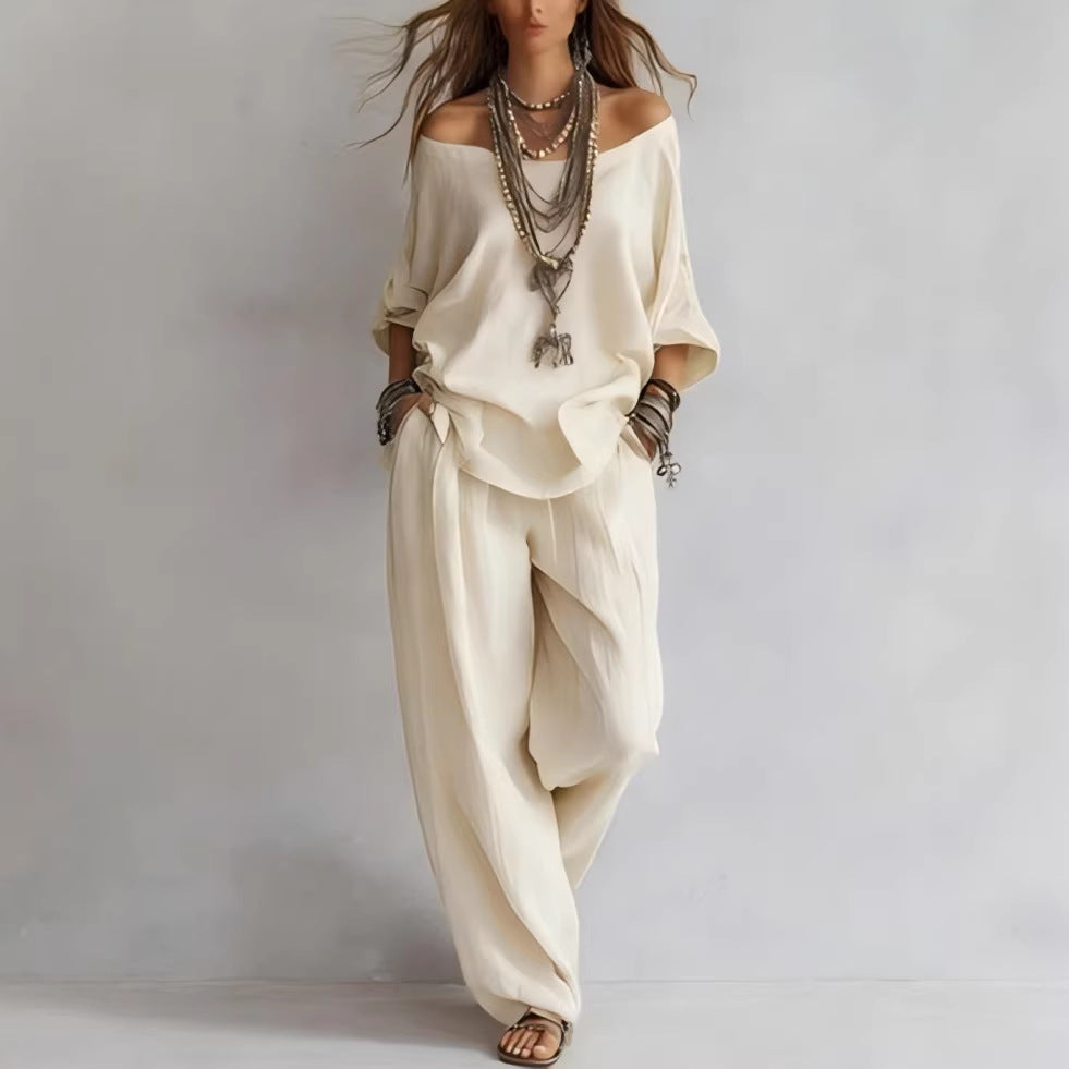 Person wearing a loose-fitting beige outfit with layered necklaces on a plain background