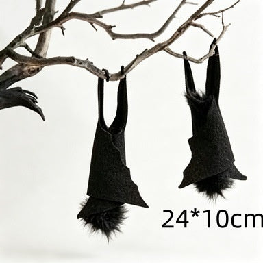 Black bat-shaped wall hanging decorations with fluffy faux fur, hanging from bare tree branches against a white background, with a size marker reading 24*10cm.