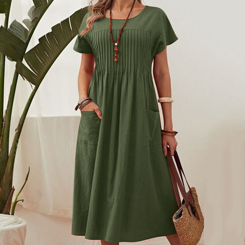 Woman wearing a green dress holding a straw bag indoors.