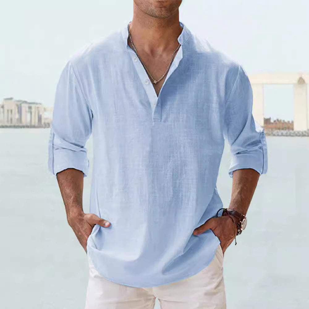 Man wearing a light blue shirt with rolled-up sleeves against a blurred outdoor background