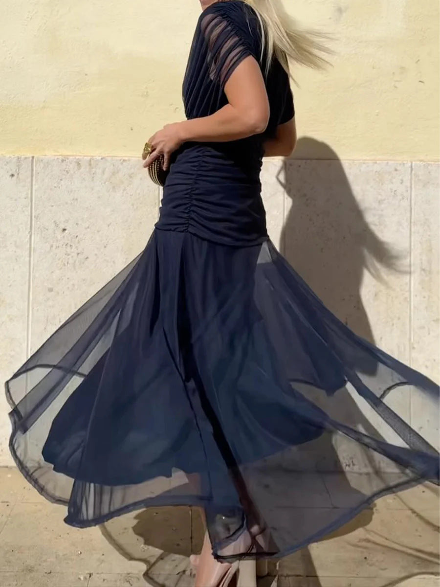 Woman wearing a flowing navy blue dress against a light-colored wall.
