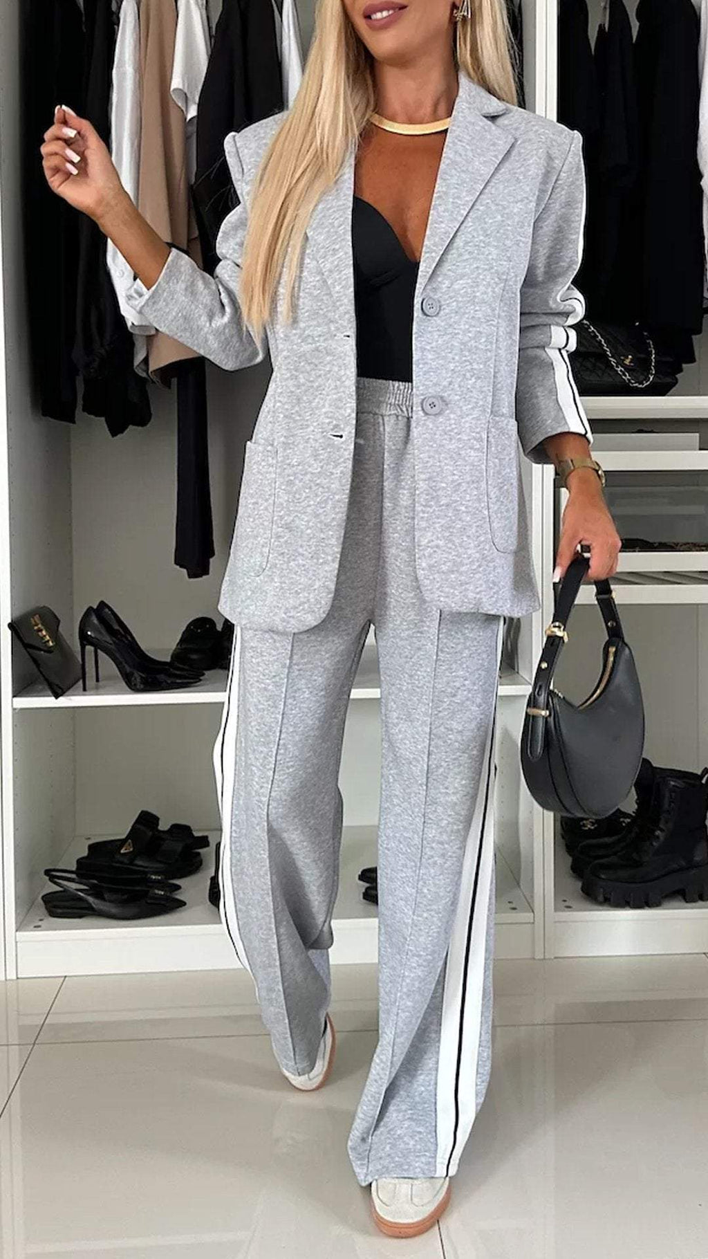 Woman in a gray suit standing in a room with shelves and shoes.
