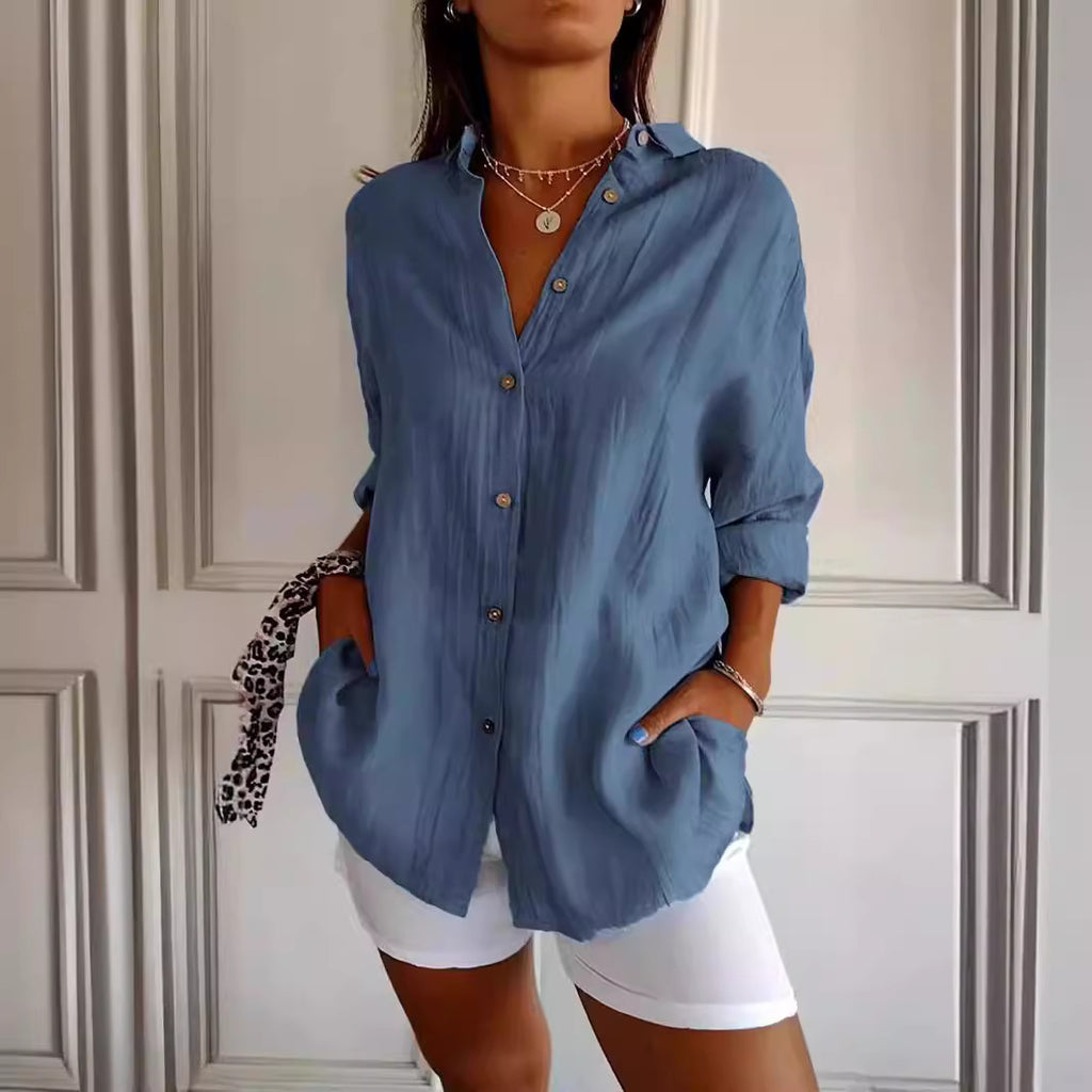 Woman wearing a blue button-up shirt and white shorts against a neutral wall.