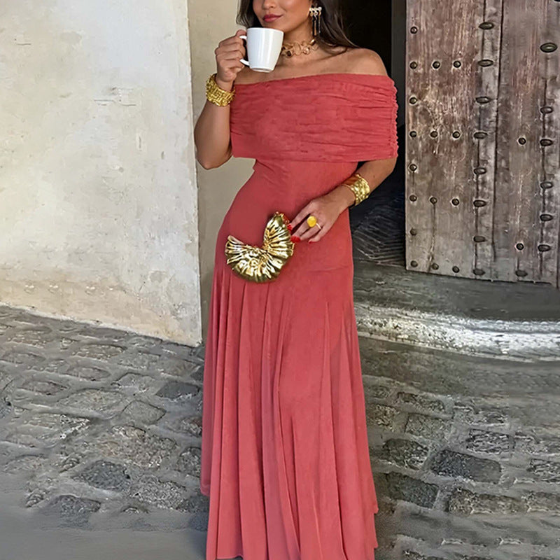 Woman in a red off-shoulder dress holding a white cup and gold clutch in front of a stone wall.