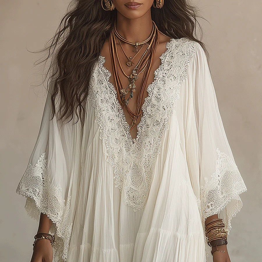A woman wearing a flowing cream-colored bohemian-style dress with intricate lace trim and wide bell sleeves, accessorized with layered necklaces and bracelets.
