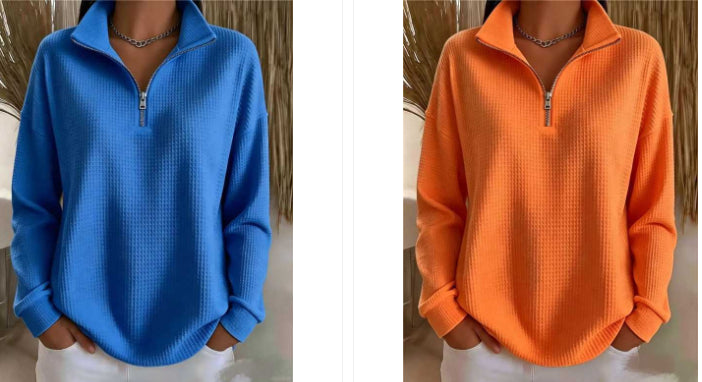 A side-by-side comparison of two women wearing waffle-knit quarter-zip pullovers, one in bright blue and the other in bright orange, both styled with white pants and a silver chain necklace.