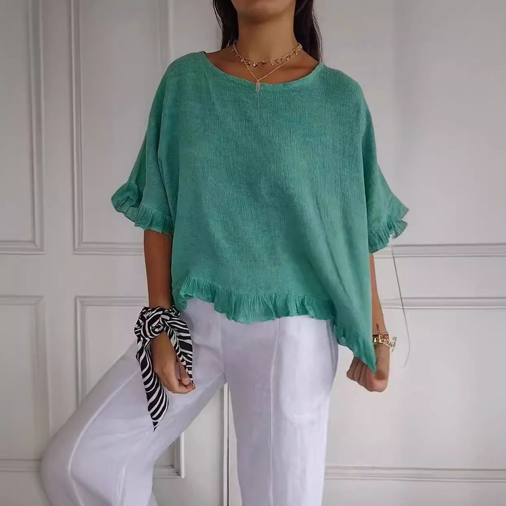 Person wearing a green top and white pants against a white paneled wall.