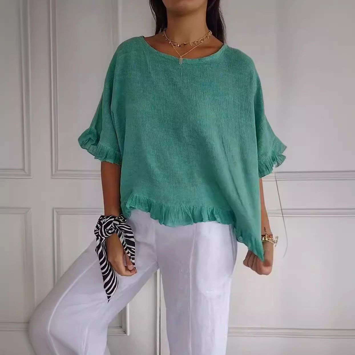 Person wearing a green top and white pants against a white paneled wall.