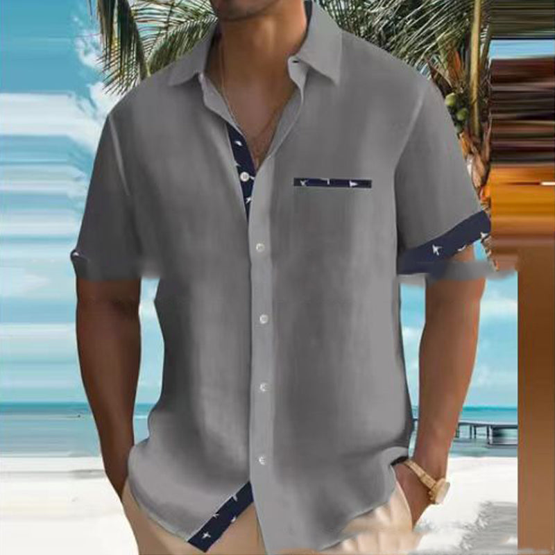 Man wearing a gray short-sleeve shirt with blue accents by a beach.