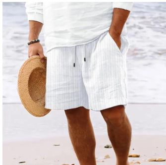 Person wearing white shorts and holding a straw hat on a beach.