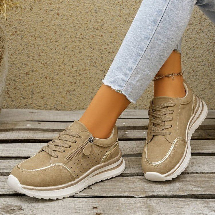Beige sneakers worn with light blue jeans on a wooden surface.