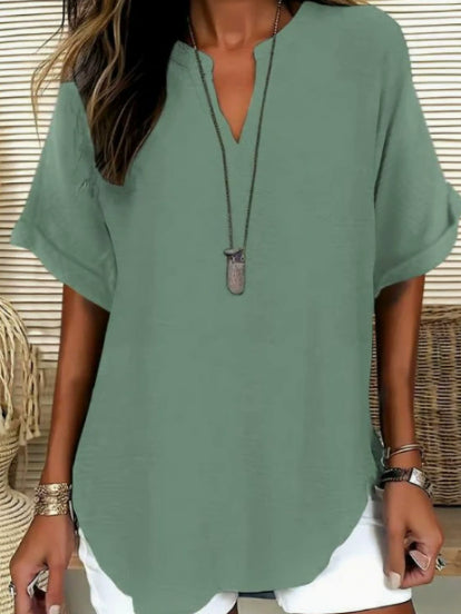 Person wearing a green blouse with a necklace, sitting on a woven chair.