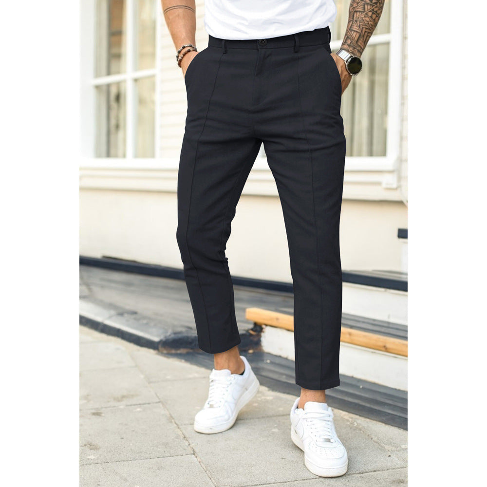 Person wearing black pants and white sneakers standing on a sidewalk.